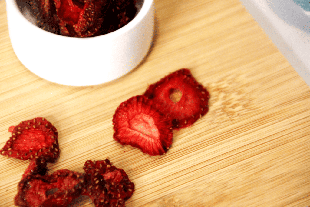 dehydrated strawberries in a white ramekin and on a wooden cutting board
