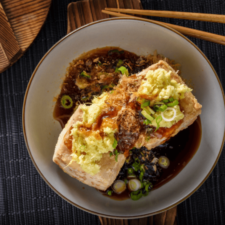 Plate of crispy air fryer agedashi tofu drizzled with tsuyu sauce and garnished with green onions.