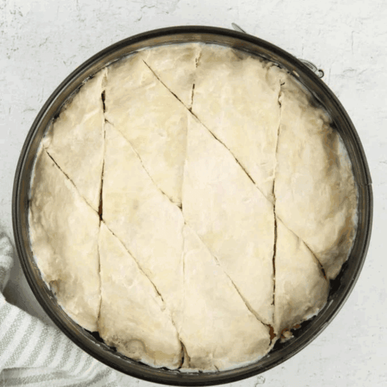 Slicing unbaked baklava into diamond-shaped pieces with a knife.