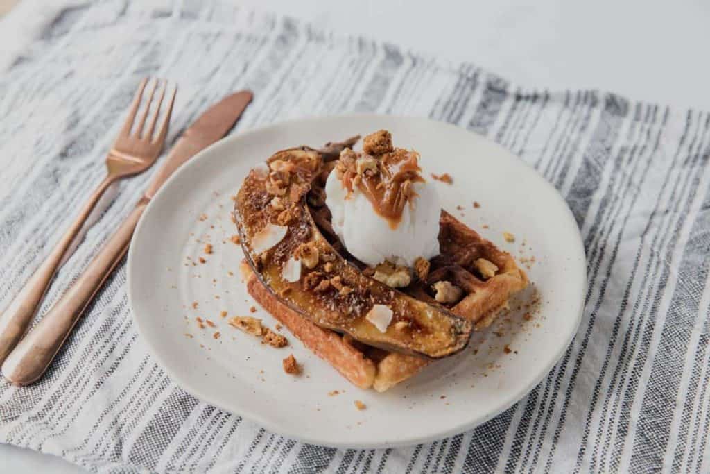 air fryer caramelized banana on top of a waffle with vanilla ice cream, caramel sauce, and chopped nuts