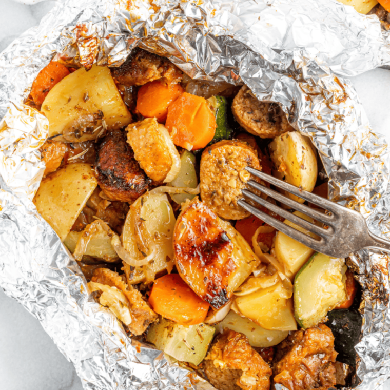 Image of the finished dish on a plate: Plate of golden brown air fryer sausage and veggies, garnished and ready to serve.