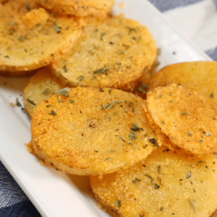 Close-up of air fryer parmesan crusted potatoes with a crisp golden cheese layer, browned edges, and fresh parsley garnish on a serving plate.