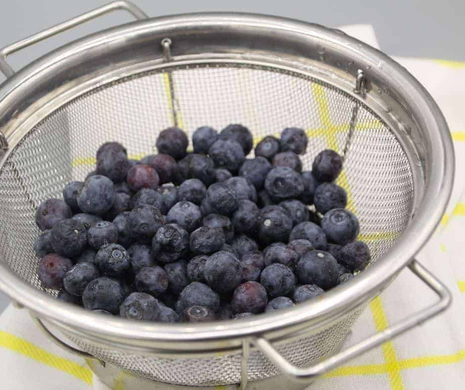 fresh blueberries in a metal colander over a yellow and white checkered towel