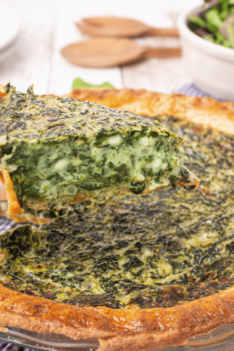 Spinach quiche slice on a plate showing creamy egg filling with spinach and melted cheese inside a golden flaky crust.