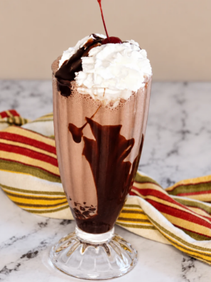 Ninja Creami chocolate milkshake in a tall glass topped with whipped cream and chocolate shavings