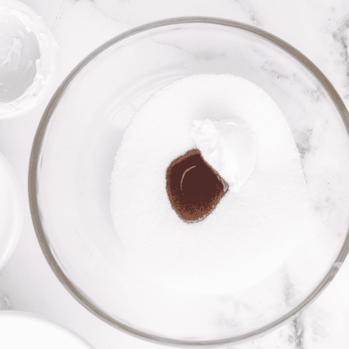 Softened cream cheese in a mixing bowl being combined with vanilla extract and granulated sugar until smooth and creamy.