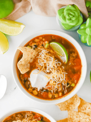 Ladling chicken enchilada soup into a bowl topped with tortilla strips, avocado, and lime