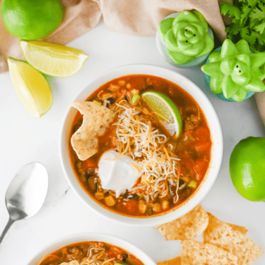 Ladling chicken enchilada soup into a bowl topped with tortilla strips, avocado, and lime