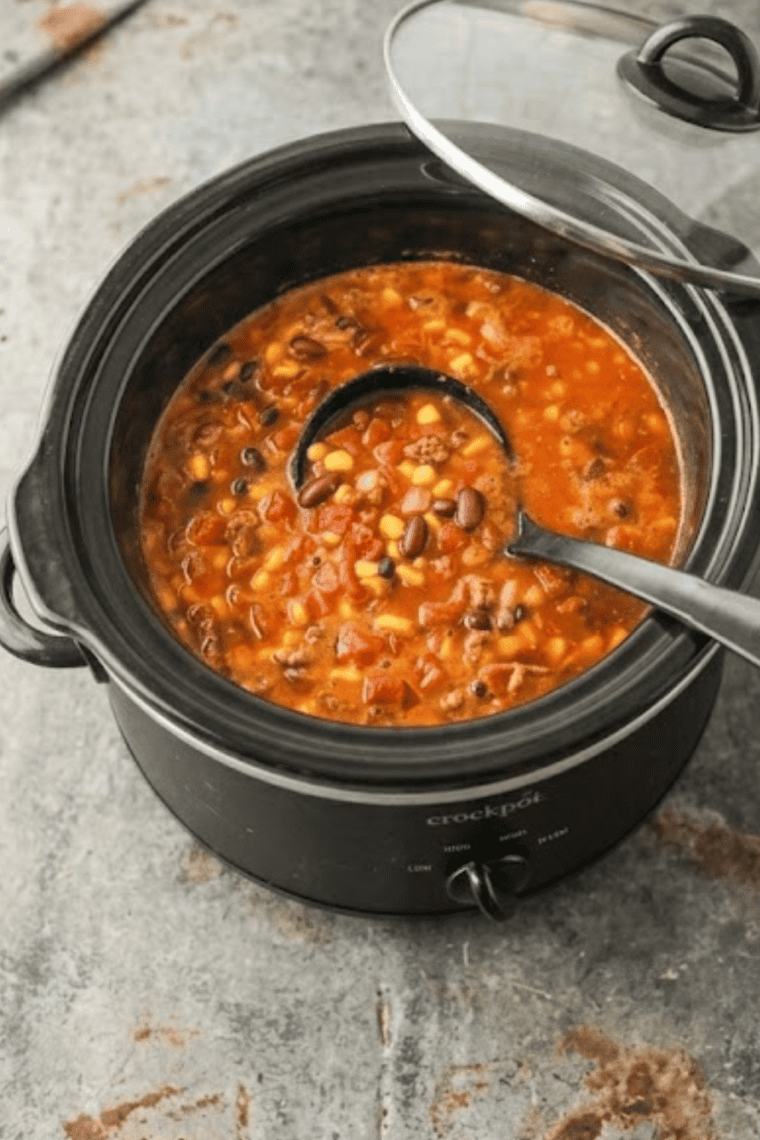 Bowl of slow cooker chicken enchilada soup with melted cheese, sour cream, and lime wedges
