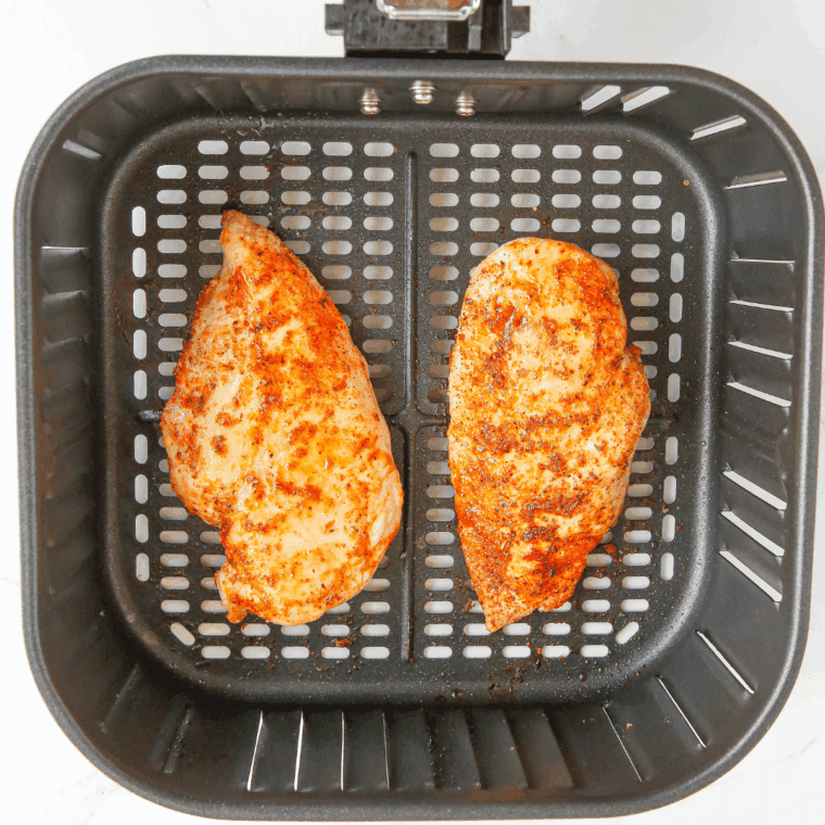 Seasoned chicken breasts cooking in an air fryer basket at 370°F, arranged in a single layer, flipped halfway through for even cooking.