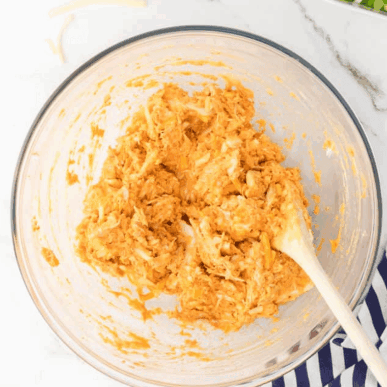 Bowl of shredded buffalo chicken cooked in the air fryer, coated in spicy buffalo sauce, ready for serving in wraps, salads, or bowls.