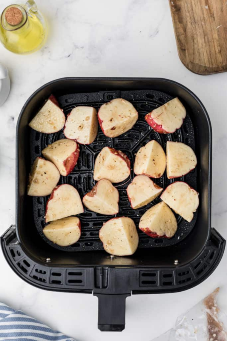 Placing seasoned potatoes in the air fryer basket.