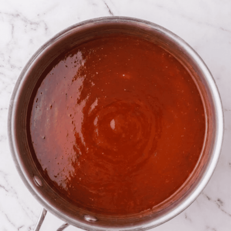 Blended preserves, vinegar, soy sauce, and spices warming together in a saucepan for sweet and sour sauce.