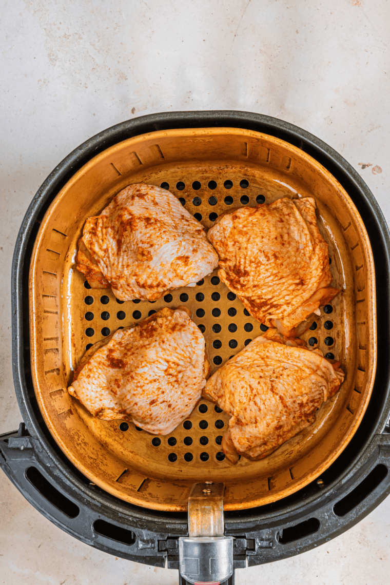 Frozen boneless skinless chicken thighs on a cutting board being patted dry with paper towels.