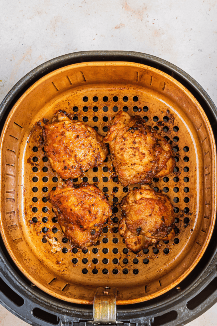 Olive oil being brushed on chicken thighs with salt, black pepper, paprika, and garlic powder sprinkled evenly.