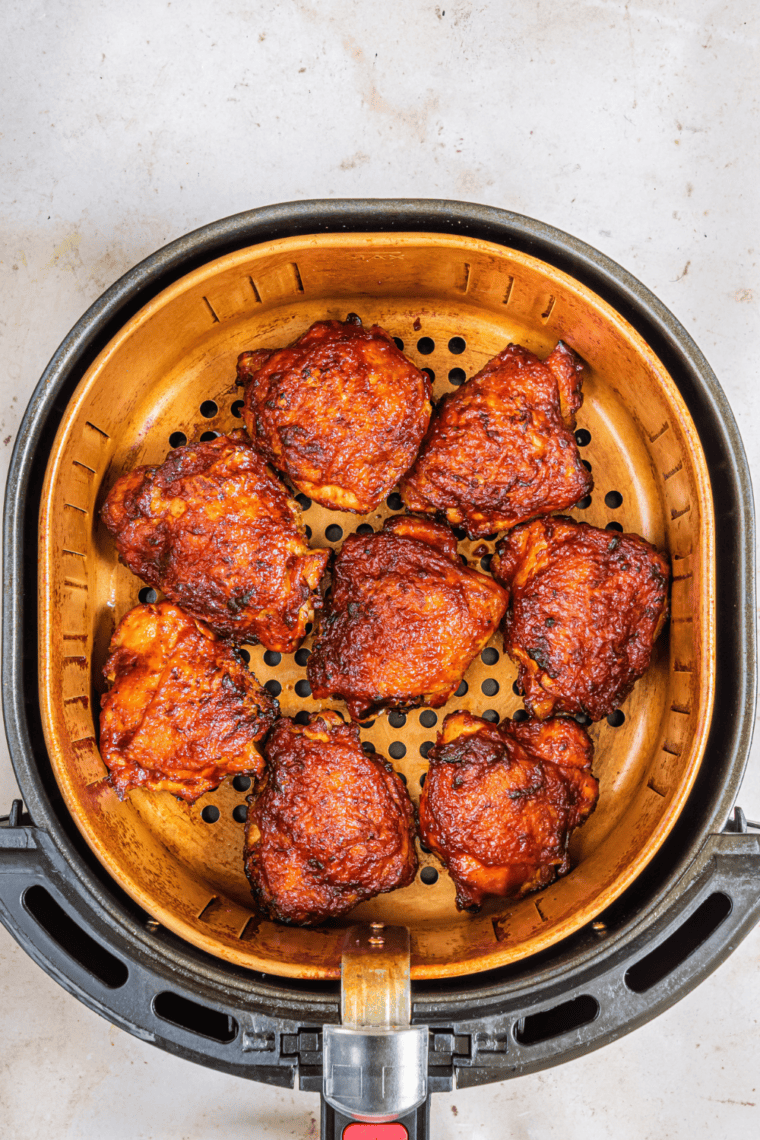 Frozen boneless skinless chicken thighs cooking in an air fryer basket, perfectly seasoned and golden brown.