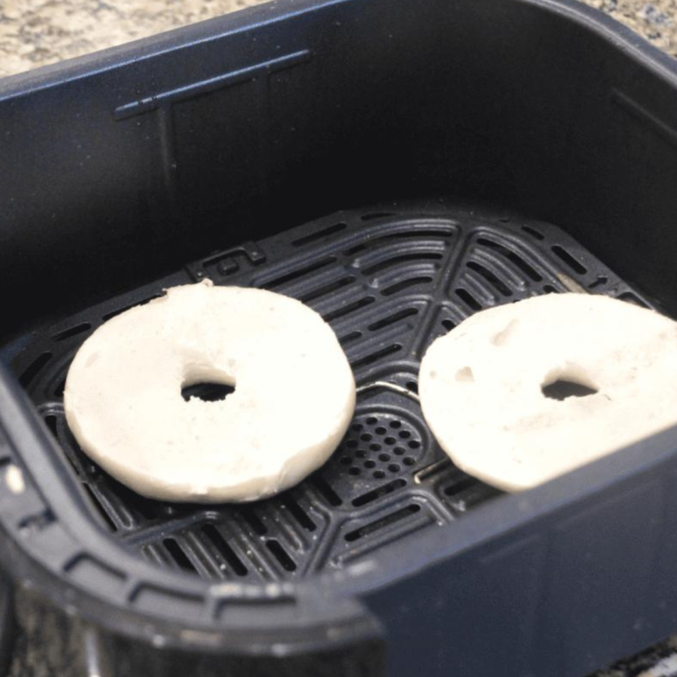 Bagels reheating in the air fryer basket, showing their golden-brown crust and warm interior