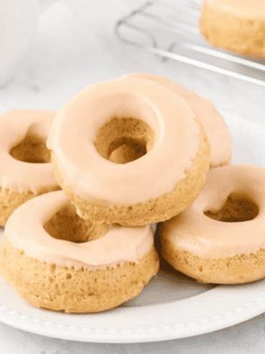 Glazed air fryer protein donuts stacked on a white plate with one showing a bite taken out