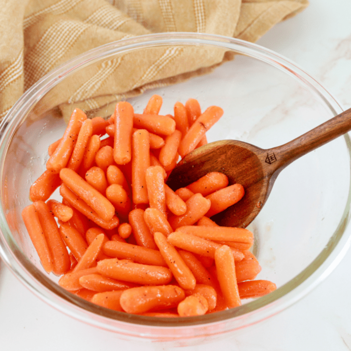 Baby carrots drizzled with olive oil and sprinkled with seasonings in a mixing bowl.