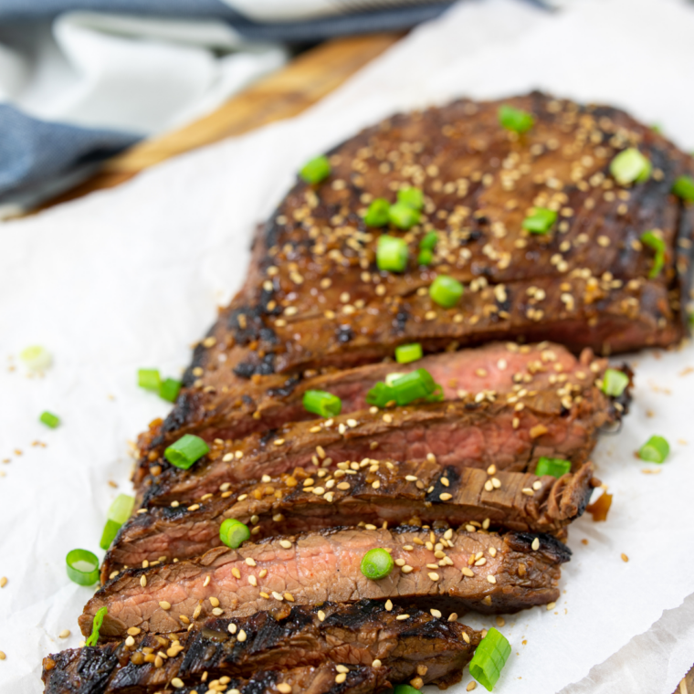 Cooked flank steak resting on a wooden board after being removed from a Blackstone griddle.