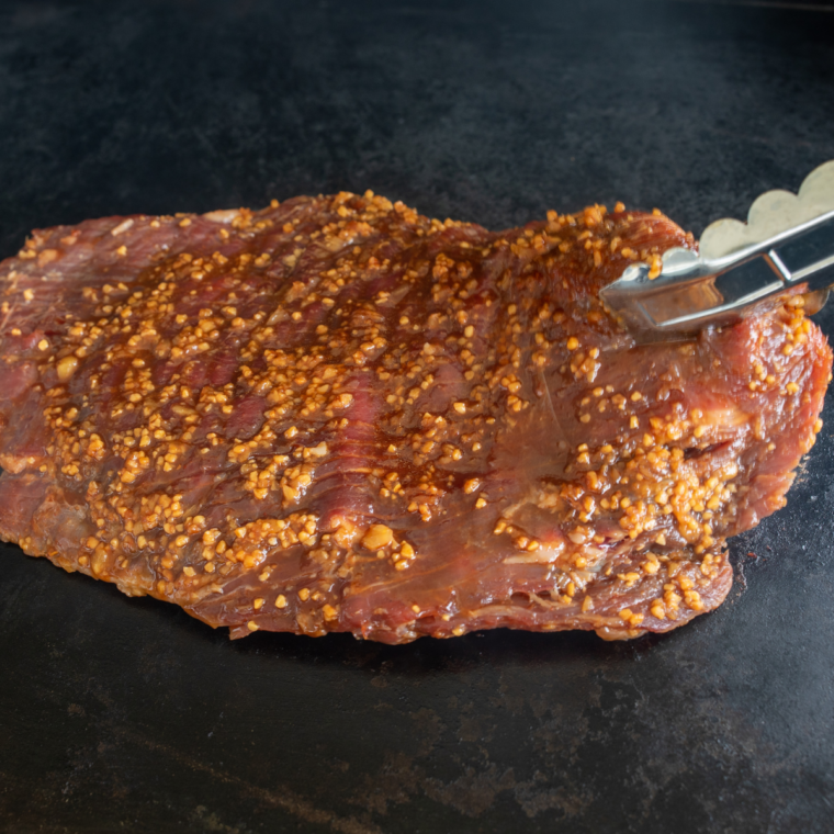 Steak being seasoned with salt and pepper and lightly oiled on hot Blackstone griddle surface