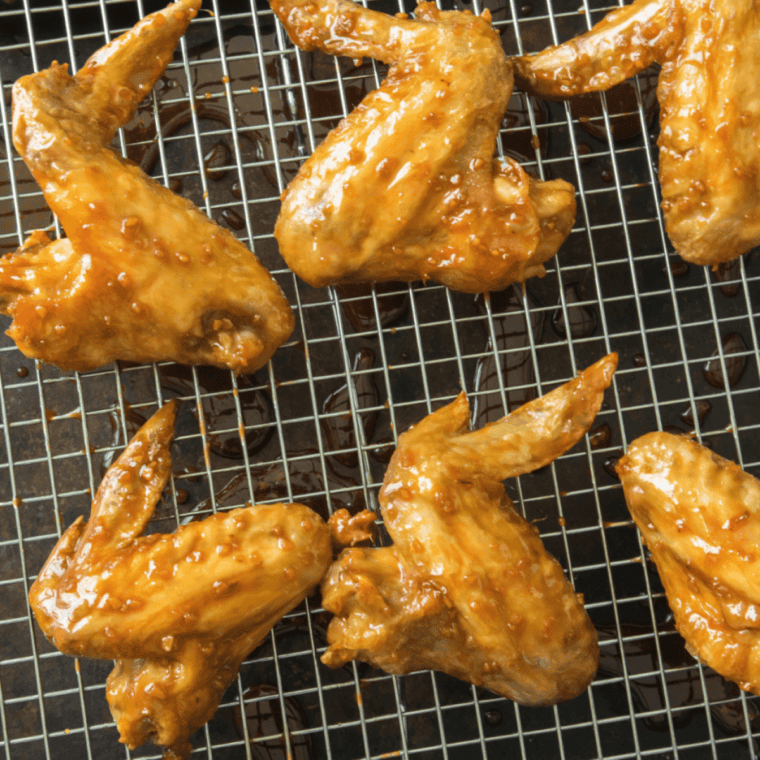 Crispy spicy garlic chicken wings coated in glossy sauce served with celery and dipping sauce on a plate.