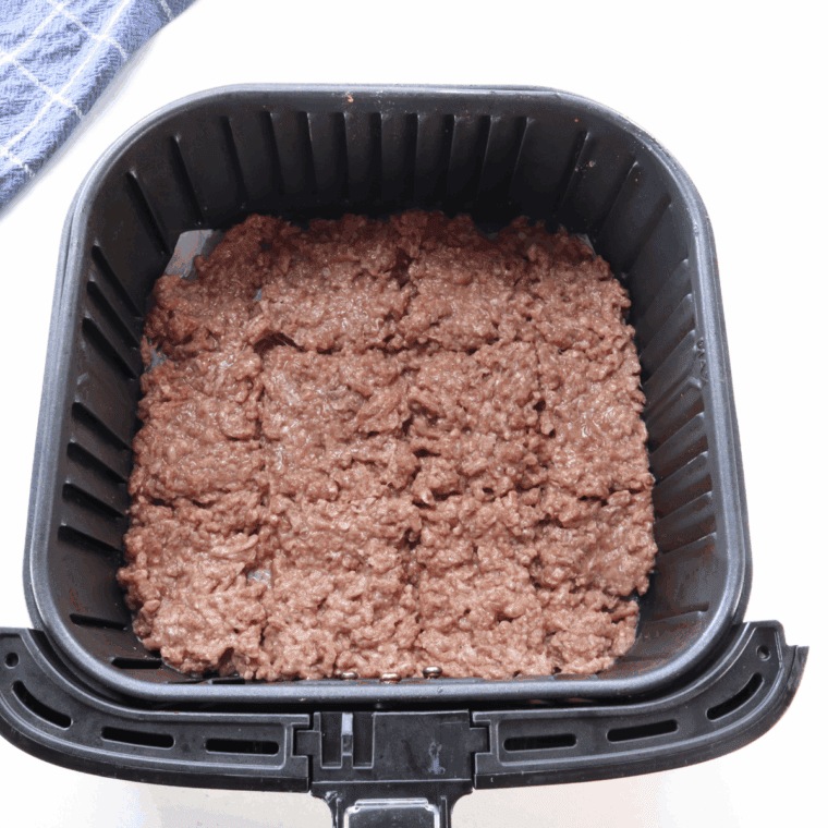 Cooking raw ground beef in the air fryer basket.