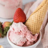 Bowl of creamy strawberry ice cream made with condensed milk, topped with fresh strawberry slices.