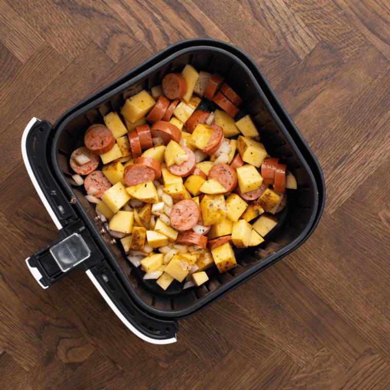 Potatoes and kielbasa in air fryer basket. 