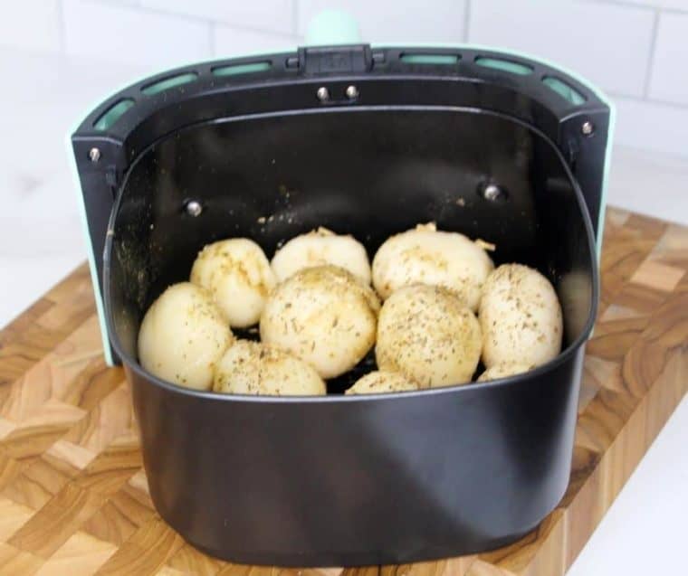 Potatoes in an air fryer basket showing how to air fry canned potatoes. 