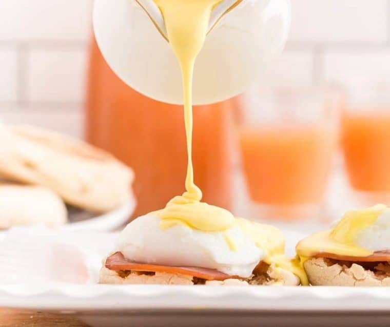 Photo of poached eggs in the air fryer on top of an English muffin being topped with Hollandaise sauce. 