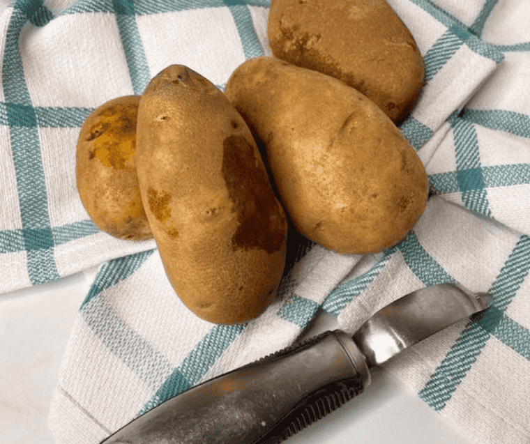 Whole potatoes and a vegetable peeler preparing for this potato peel recipe. 