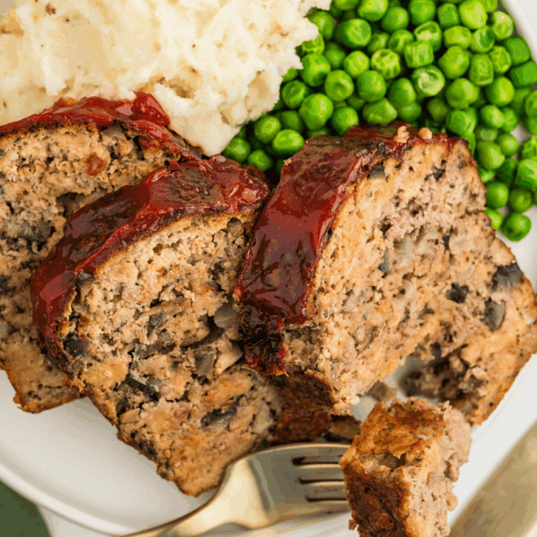 Assorted savory side dishes served with hearty slices of meatloaf on a dinner plate.