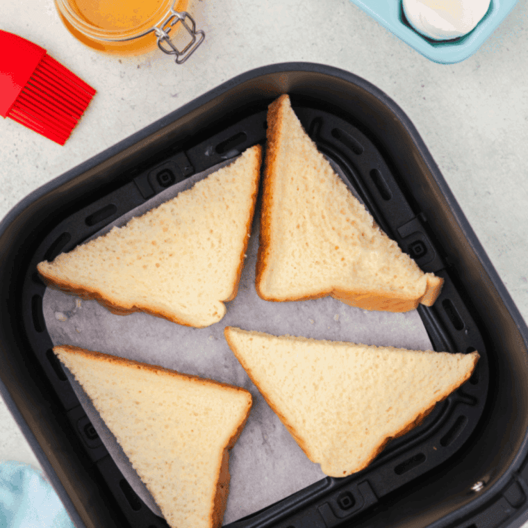 Placing the egg-coated bread slices into the air fryer and setting the timer, flipping halfway through cooking.