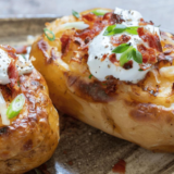 Cooked jacket potato topped with cheese, sour cream, and chives on a plate.