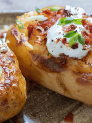 Cooked jacket potato topped with cheese, sour cream, and chives on a plate.