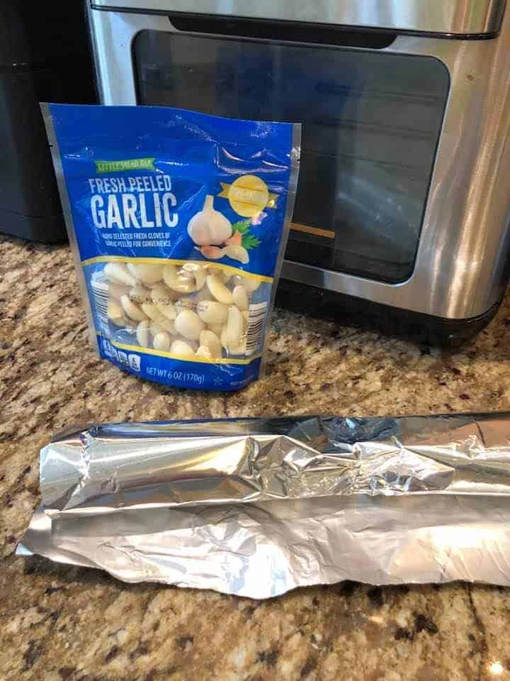 Foil, fresh peeled garlic, and air fryer to show what you need for roasting garlic in air fryer. 