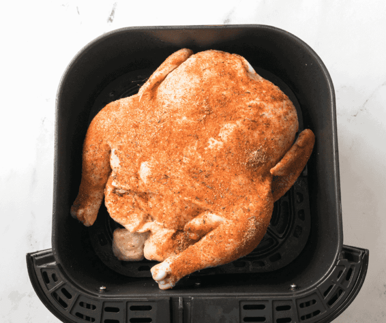 whole chicken coated in spices in air fryer basket