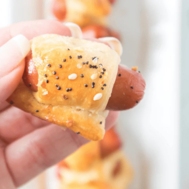 Hand holding an air fryer bagel dog dipped in mustard