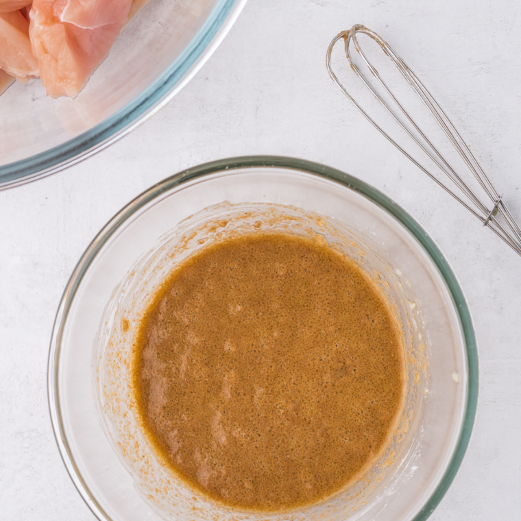 Combining chicken with marinade ingredients in a bowl and refrigerating while preparing vegetables and sauce.