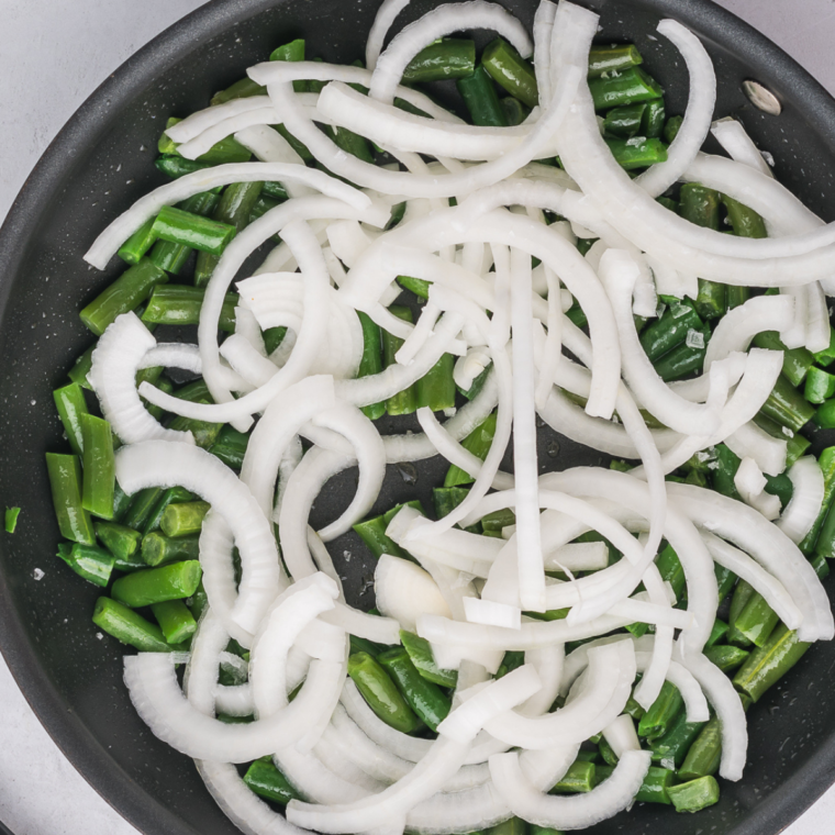 Heating oil in a skillet, sautéing green beans and onions with salt until onions are translucent.