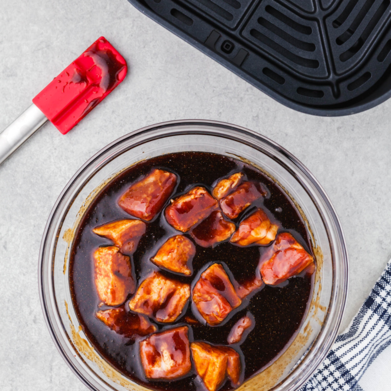 Seasoning raw pork belly cubes with salt, pepper, garlic powder, and smoked paprika in a glass mixing bowl