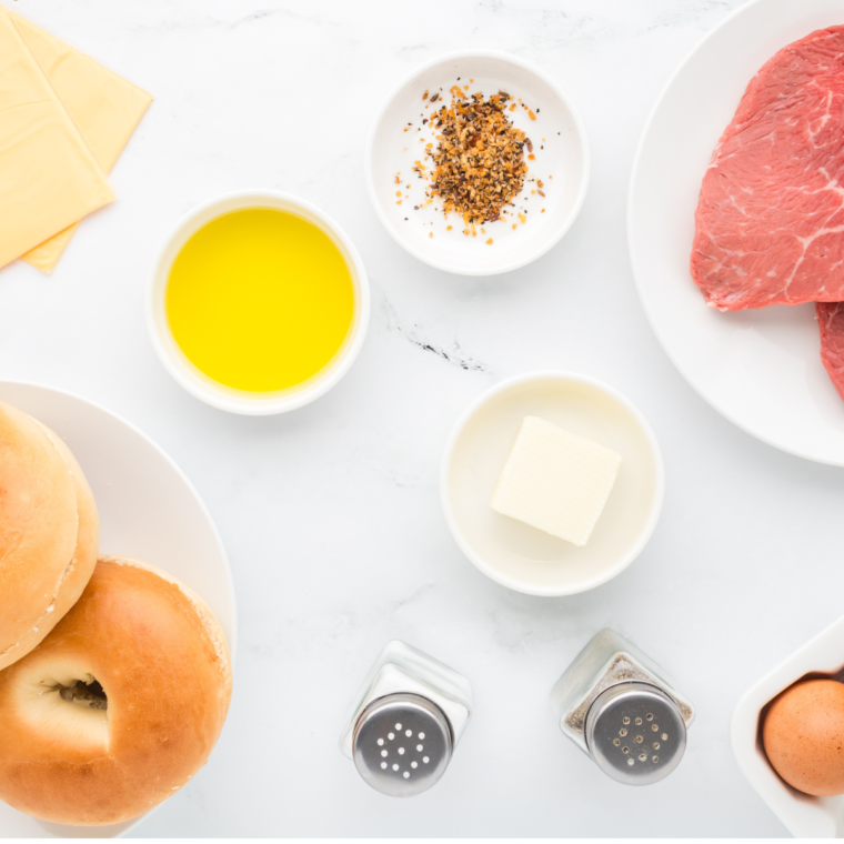 "Ingredients for Copycat McDonald’s Steak, Egg, and Cheese Bagel Recipe displayed on a wooden table, including steak, eggs, cheese, and bagels."