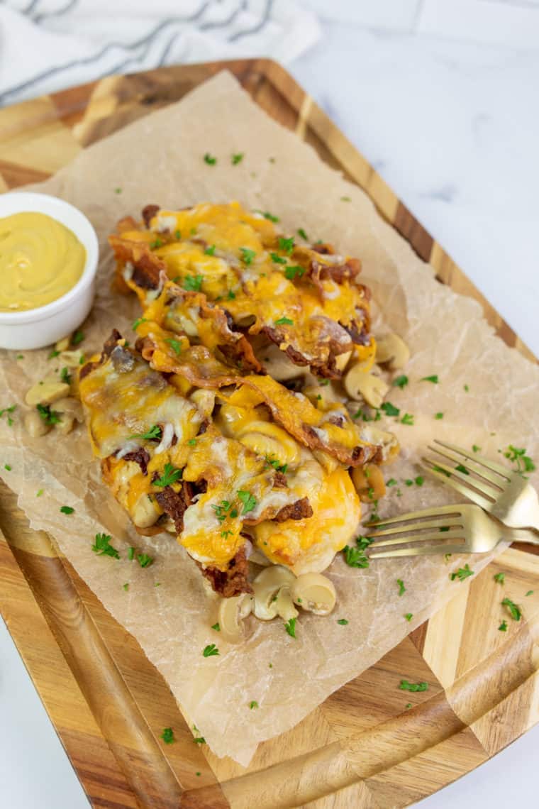 Plate of Outback Steakhouse Alice Springs Chicken topped with melted cheese, crispy bacon, sautéed mushrooms, and fresh parsley.