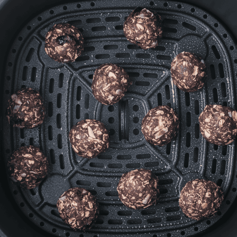 Spraying protein balls with cooking spray to prevent sticking before air frying.