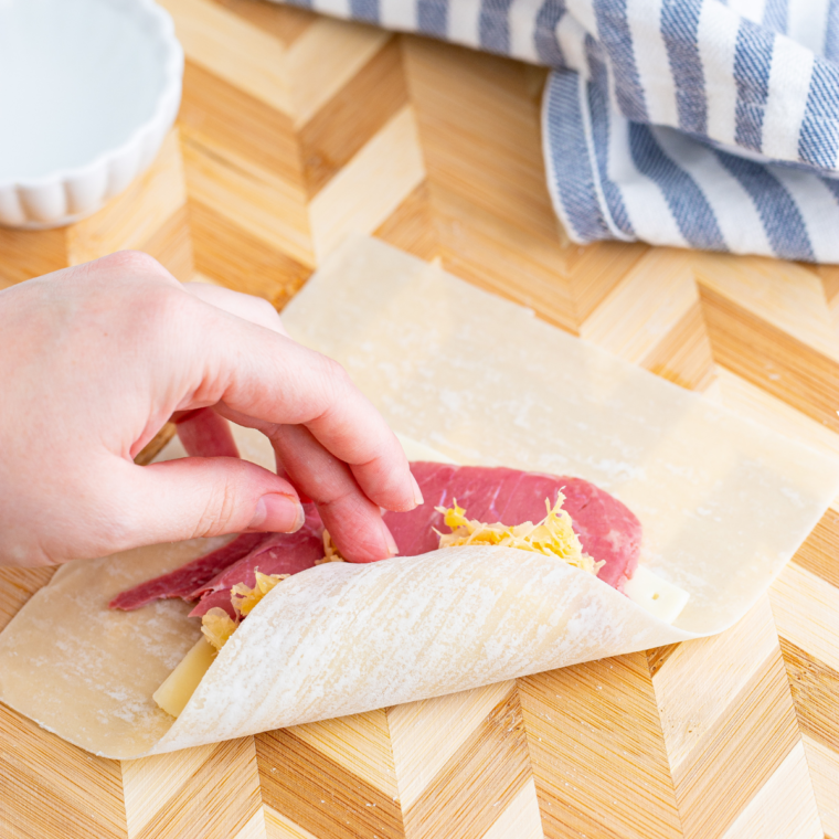 Egg roll wrapper topped with Swiss cheese, corned beef, and sauerkraut mixture, ready for rolling.