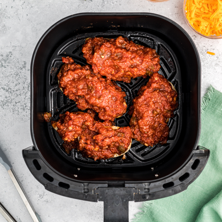 Chicken breasts placed in the air fryer basket, coated in salsa and seasonings, cooking to juicy perfection.