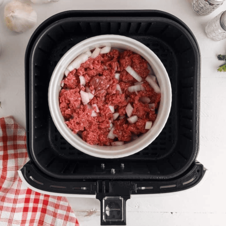 Ground beef and diced onions cooking in a casserole dish inside an air fryer basket