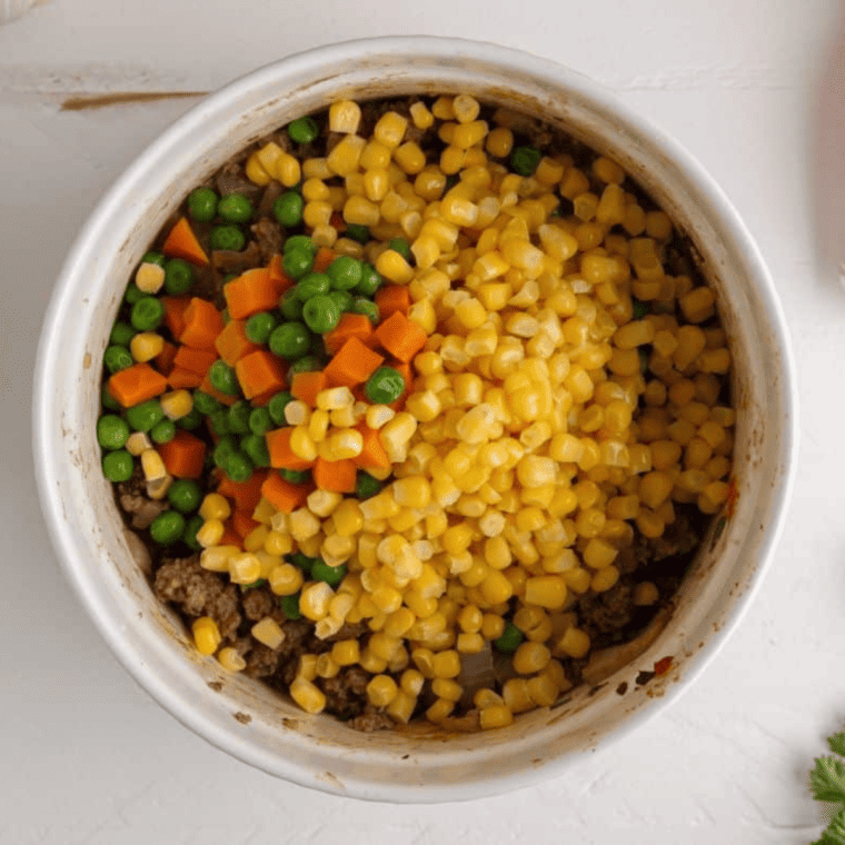 Cooked ground beef mixed with vegetables, broth, tomato paste, and seasonings in casserole dish