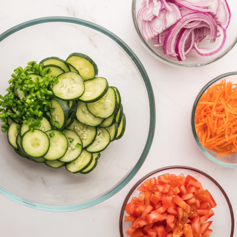 Combining tomatoes, cucumber, onion, carrots, lime juice, and soy sauce in a large bowl.